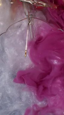 Dikey video. Parıltılı duman. Boya karışımı. Gümüş rengi, pırıl pırıl parlayan mürekkep dumanı, kıvrılan karanlık suyu damlatıyor. Soyut arkaplan parçacıkları kırık cam ampul.