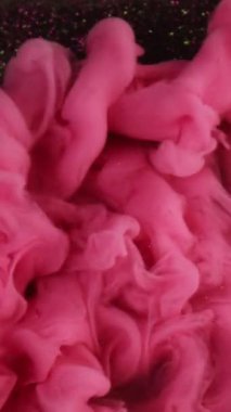 Dikey video. Sis dalgası. Pembe duman. Parlak bulutlar parıltılı karanlık yüzey boyunca yayılır. Boya spreyi. Suyun soyut arka planında karmaşık kıvrımlarla süslenmiş..