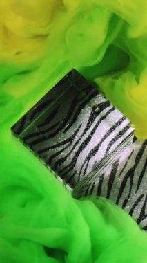 Dikey video. Boya patlaması. Parlak buhar. Odaklanmamış yeşil, çok renkli duman kübü. Soyut desenli sanat arka planına mürekkep dokusu sıçratıyor..