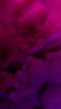 Dikey video. Sanat sıvısı. Duman boyası. Mor pembe parıltı dalgası sıvı karışımı neon rengi ışıltılı arka plan su bulanık spot ışığı lensi.