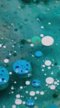 Dikey video. Boya jeli. Yağ kabarcıkları. Turkuaz pigment topları saydam bulanık sanat sıvısı mermer mavi su soyut arka plan derinliğinde yüzüyor.