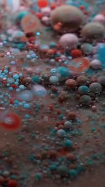 Dikey video. Köpüklü sis. Pigment dökülmüş. Küçük yuvarlak renk parçacıkları bulanık şeffaf sıvıda yüzen boyaları karıştırıyor. Petrol sanatı suyu soyut arkaplan.