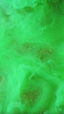 Dikey video. Boya sıvısı. Canlı bir sıçrama. Odaklanmamış yeşil renk sisi, buhar, soyut ışıldayan sanat arka planında ışıldıyor..
