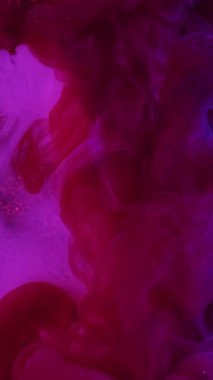 Dikey video. Çok renkli duman. Boya dumanı. Mor bukleli hava akışı parlak pembe soyut su arka planında. Mistik mürekkep sarmallarının hafif salınımları.