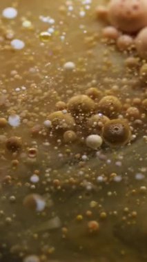 Dikey video. Kabarcık akışı. Akrilik kütle. Sarı kahverengi boya ile şeffaf doku sıvısı tüttürmek parçacıkların etrafında patlamış sanat tozu soyut arka plan.