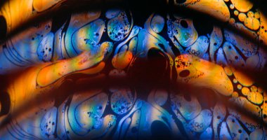 Parlak kemer bulanıklığı. Gökkuşağı sabunu akışı. Mavi turuncu, siyah arka planda, yuvarlak ışık lensi. Soyut sıvıyı harmanlayan renk mürekkebi.