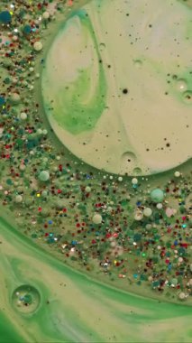 Dikey video. Akrilik kütle. Boya karışımı. Parıldayan metal parçacıkları yeşil suda yüzüyor. Soyut odaklanmış nem kabarcığı patlaması arkaplanı.