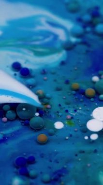 Dikey video. Renkli akış. Kabarcık boyası. Su yağı karışımı pigment damlası patlıyor. Mavi beyaz parçacıkları dolduran dalga koyu soyut arkaplan.