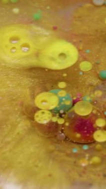 Dikey video. Parıltı akıyor. Kabarcık patladı. Renkli pırıl pırıl altın sıvısı ve yuvarlak jel dökülmüş. Sarı pembe leke parlak su soyut arkaplan.