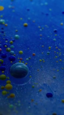 Dikey video. Mavi akış. Kabarcık emülsiyonu. Parlayan suda yüzen çok renkli akrilik küreler. Soyut arkaplanda mürekkep damlası karışımı.