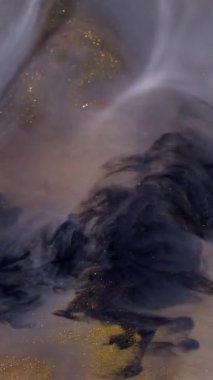 Dikey video. Mürekkep döküldü. Parıldayan sıvı. Odaklanmamış siyah gri, altın rengi parıldayan, nemli boya karışımı, soyut sanat arkaplanı. Parlak dumanlı yüzey.