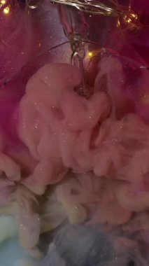 Dikey video. Parıltılı akış. Boya patladı. Çok renkli duman kıvrımları garip bir şekilde ışıl ışıl sanat sıvısı arka planlarını karıştırıyor. Peçe dumanı pembe su ampulü kırıldı..