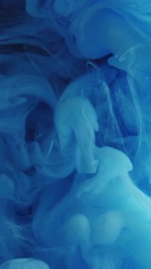 Dikey video. Sis dalgası. Mavi duman. Pürüzsüz gizemli boya karışımı bulut. Suluboya, suda çözünen tuhaf buklelerin soyut arka planında çözünür.