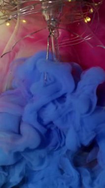 Dikey video. Renkli duman. Kırık yüzey. Duman sanatı mavisi pembe mürekkep sıvısı soyut arkaplan suyunu eski cam ampullerle yayar..