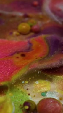 Dikey video. Işıldayan akış. Parlak boya damlası. Renkli akrilik jel köpüklü barut suyuna dökülüyor. Yeşil pembe sıvı karışımı soyut arkaplan.