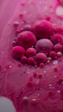 Dikey video. Boya jeli. Yağ kabarcıkları. Pembe pigment topları saydam bulanık sanat sıvısı mermer içinde yüzüyor. Suyun soyut arkaplanı parıldıyor. .
