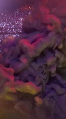 Dikey video. Duman patlaması. Pigment akışı. Işıldayan soyut arka plan çözünmüş su lensi üzerinde parlak renkli toz boya bulutu.