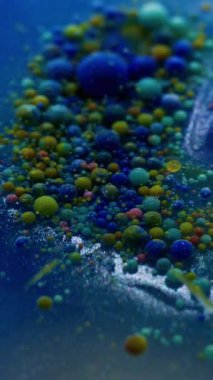 Dikey video. Yağ sıvısı. Su damlasını boya. Mavi suda yüzen odaksız renkli kabarcıklar. Patlayan jel dokusu serumu soyut sanat arkaplanı.