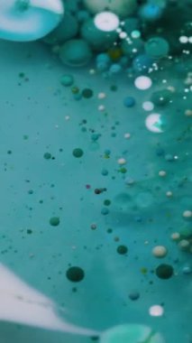 Dikey video. Köpüklü sis. Pigment dökülmüş. Yuvarlak turkuaz mavi parçacıklar bulanık şeffaf sıvıda boya dökülmesini karıştırıyor. Petrol sanatı suyu soyut arkaplan.
