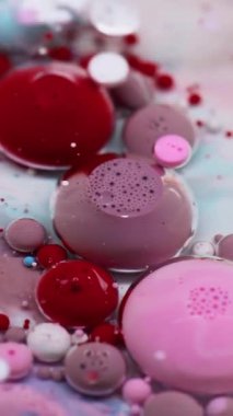 Dikey video. Baloncuk döküldü. Mürekkep akışı. Yağ rengi damlaları suda çözünüyor. Kırmızı pembe beyaz akrilik pigmeler köpük soyut sanat arka planı.