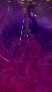 Dikey video. Mürekkep simleri. Dumanlı akış. Işıldayan hipnotik pembe dalgalı dalgalar küçük parlak parçacıkların içinde karışıyor. Bulutlu renk akış arkaplanı.