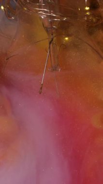 Dikey video. Parlak duman. Sanat sıvısı. Parlak renkli arka planda turuncu boya şişmesi. Dalgalı karışım bulut parçacıkları kırık lamba.