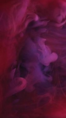 Dikey video. Soyut boya. Renkleri karıştırıyorum. Odaklanmamış kırmızı sis mürekkep dokusu buhar sıvı duman bulutu sanat arka planında ışıldıyor.