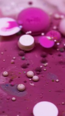 Dikey video. Boya akışı. Kabarcık emülsiyonu. Canlı pembe beyaz su karışımı yüzen renkli damlalar patlama dokusu. Dalgalar soyut arkaplanı doldurur.