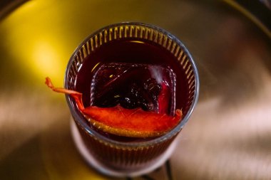 Negroni camı. Alkolik içki. Kırmızı kokteyl buz küpü turunçgil dilimi kabuğuyla servis ediliyor. Bar tezgahında serinletici bir içki karışımı..