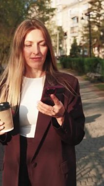 Dikey video. Konuşan kadın. Modern teknoloji. Kahveli, mutlu, şık bir iş kadını dışarıda telefonla konuşuyor..