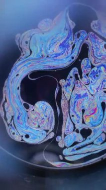 Dikey video. Gökkuşağı küresi. Yağ pigmenti. Odaklanamayan siyah arkaplanda renkli yuvarlak lens. Soyut yüzen benzin neon mürekkep karışımı sıvı..