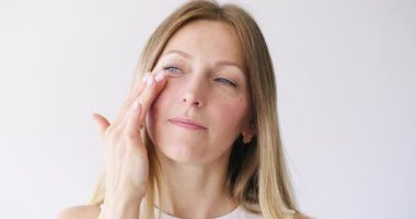 Yüz güzelliği. Cilt nemlendirici. Rahatlamış sakin kadın beyaz fotokopi arkaplanına krem sürerek cilt bakımı yapıyor..