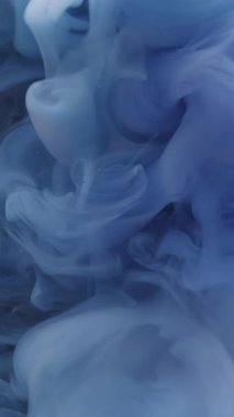 Dikey video. Puslu bir arkaplan. Soyut boya. Suyun içindeki mavi renkli ruhani duman dokusu yaratıcı sanata yayılıyor..