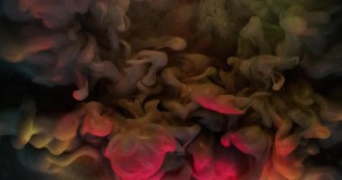 Boyalı su. Soyut sim sisi. Odaklanmamış turuncu pembe renkli bulut parçacıkları gökkuşağı resimleri koyu siyah arka planda yayılıyor..