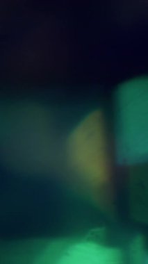 Dikey video. Bokeh enerjisi. Bulanık ışın soyut. Odaklanmamış yeşil mavi, çok renkli, yanıp sönen ışık merceği deseni koyu siyah arkaplanda..