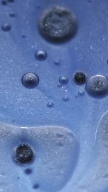 Dikey video. Köpük sıvısı. Yağ sıvısı dokusu. Soyut sanat akrilik zemin üzerinde yüzen su yuvarlak parlak mürekkep damlasına odaklanmış mavi renk boyası.