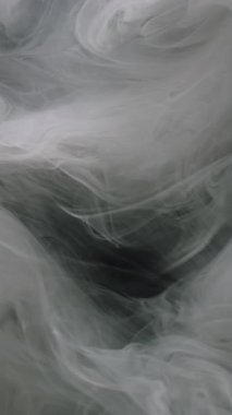 Dikey video. Duman boyası. Buhar bulutu. Odaklanamayan sisli doku su patlaması akışına mürekkep sıçratır soyut sanat üzerine yayılan koyu siyah arkaplan.