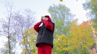 Sonbahar parkının arka planında bir çocuk bardaktan sıcak bir içecek içer..