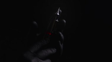 Kalıcı kaş, dudak ve kirpiklerden oluşan siyah steril eldiven ustasının elleri. Siyah arka planda, usta bir dövme makinesi tutuyor, lambayla aydınlatılıyor.