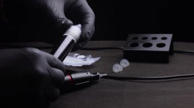 Kalıcı kaş, dudak ve kirpiklerden oluşan siyah steril eldiven ustasının elleri. Usta, kalıcı makyaj için dövme pigmentindeki beyaz başlığı söker.