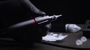 Kalıcı kaş, dudak ve kirpiklerden oluşan siyah steril eldiven ustasının elleri. İşyerinde, usta dövme makinesini elleriyle çevirir ve her taraftan onu gösterir, kalıcılığın lambası.