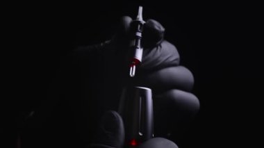 Kalıcı kaş, dudak ve kirpiklerden oluşan siyah steril eldiven ustasının elleri. Usta, dövme makinesinden kalıcı makyaj için fişeği çıkarır ve inceler. 