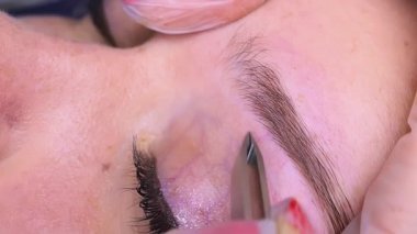 Kaş bölgesindeki istenmeyen tüyleri cımbızla yolmak. Kozmetik prosedür kalıcı kaş makyajı. Kaş dövmesi..