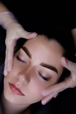 Permanent make-up of the eyebrows, close-up of the model's face, the master holds the eyebrows with his hands