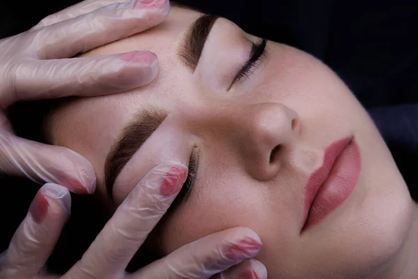 Permanent makeup of the eyebrows, the master touches the eyebrows of the model with his finger after the procedure