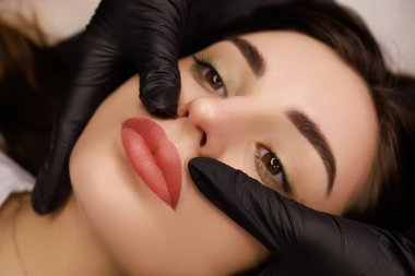 finished work of permanent makeup of the lips master in black gloves holds the lips of the model
