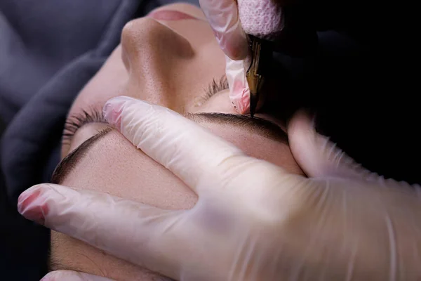 Close-up of the procedure of permanent makeup of the eyebrows, the master holds the eyebrows with his fingers and applies a tattoo on the eyebrows.