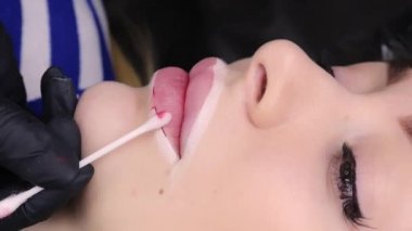 Usta, model dudakların çevresindeki kalıcı makyajın uygulanmasını pamuklu çubukla pigmenti silerek kontrol eder. Yüksek kalite 4k görüntü