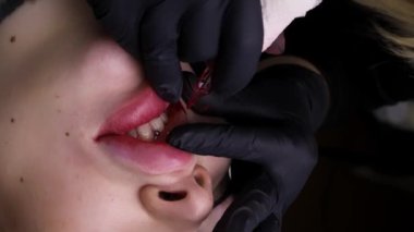 Kalıcı makyaj prosedürü üzerine yalan söyleyen güzel bir kız modelin dudaklarına yakın çekim, usta dövme makinesi ile kalıcı makyaj uygular. Yüksek kalite 4k görüntü