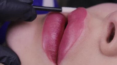 Dudakların yakın çekimi ve kalıcı makyajın uygulandığı model, teknisyen model dudakların üzerine pamuk çubuğu sürer. Yüksek kalite 4k görüntü